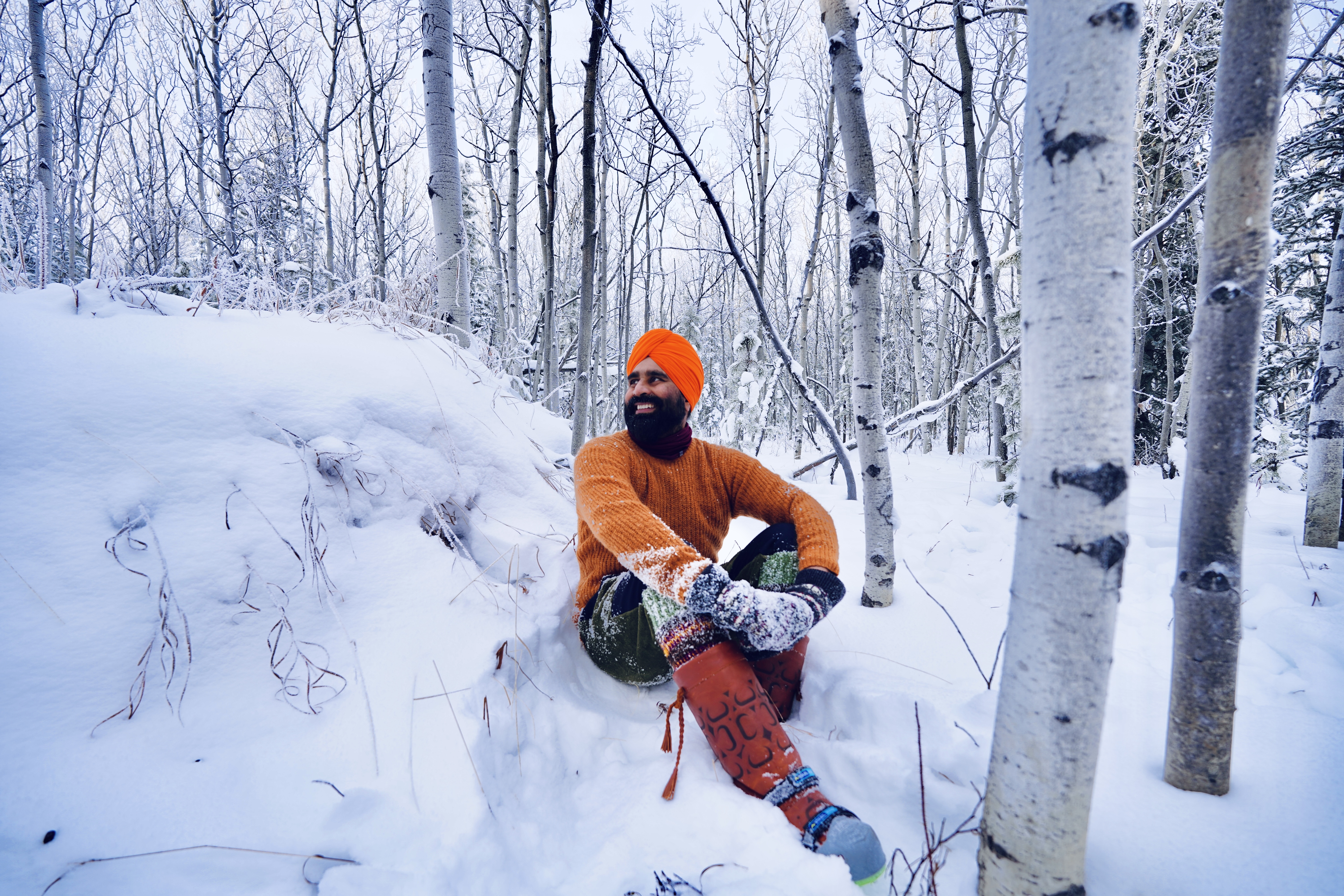 Gurdeep Pandher, wearing an orange top, sits in the snow among the trees. 