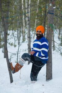 Photograph: Christian Kuntz Photography. Gurdeep seen in the snow, he rests his back against a tree and has propped hist other leg on a younger tree.